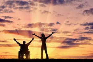 man in wheelchair and woman with their hands open in front of sunset